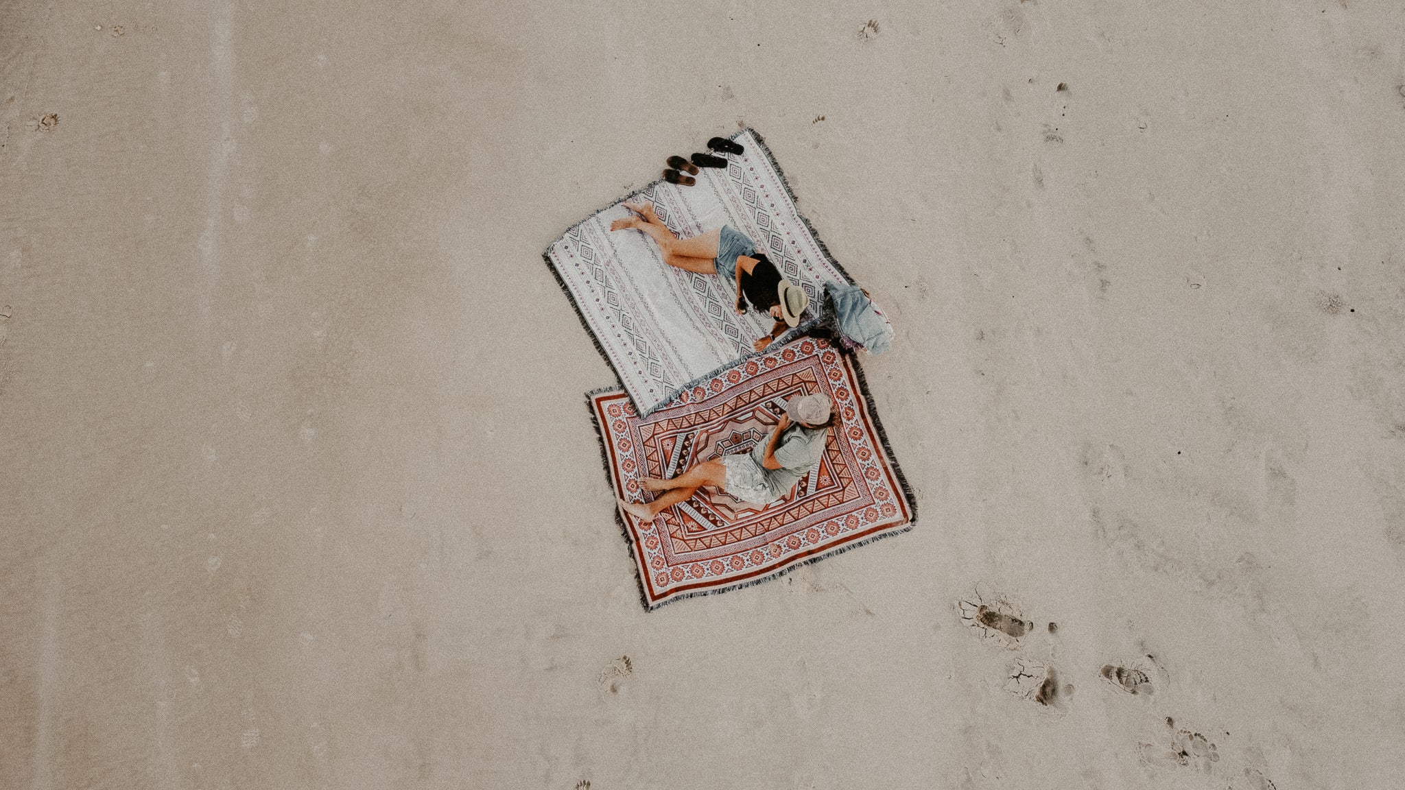 Aerial shot of boy and girl sitting on the beach on cotton throw rugs
