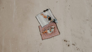 Aerial shot of boy and girl sitting on the beach on cotton throw rugs