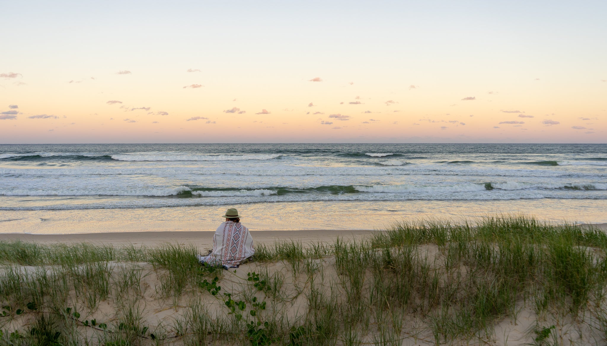 Boys sitting in Sand Dunes with rug wrapped around him watching the waves