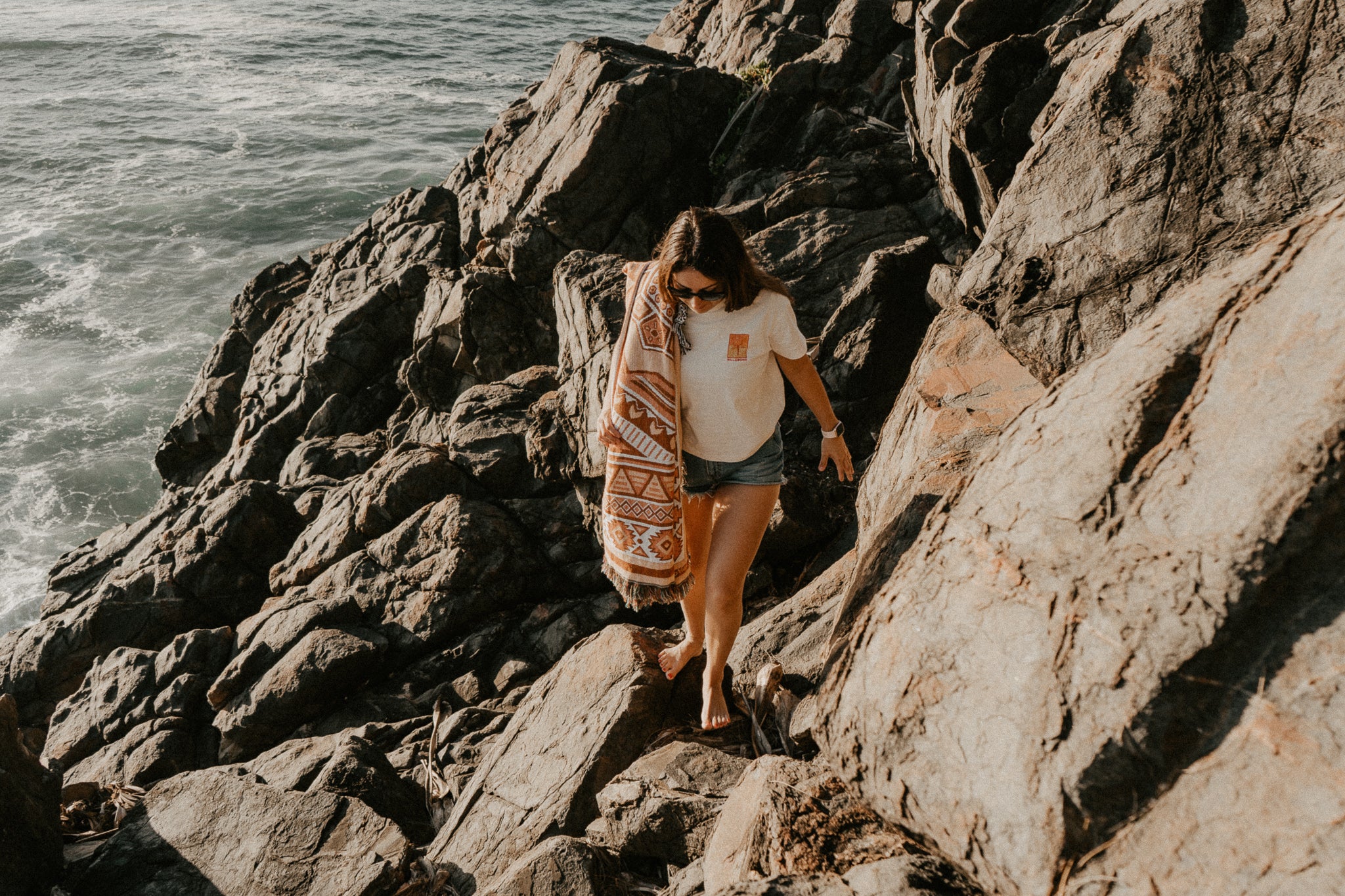 Girl walking on rocks at beach with rug on shoulder