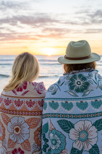 Girl & boy watching sunrise on beach with pink and green floral florence throws wrapped around them