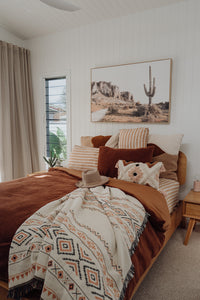 Cotton throw on bed, hat on bed, cactus picture on wall