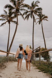 Two girls on beach, bag on cotton shoulder, palm trees in background