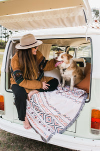 Girl and dog sit in back of vw kombi on top of white throw rug