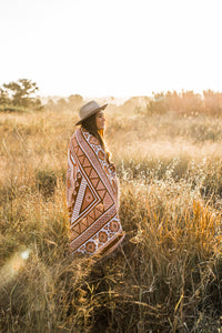 Girl in long grass field with orange sofia throw wrapped around her